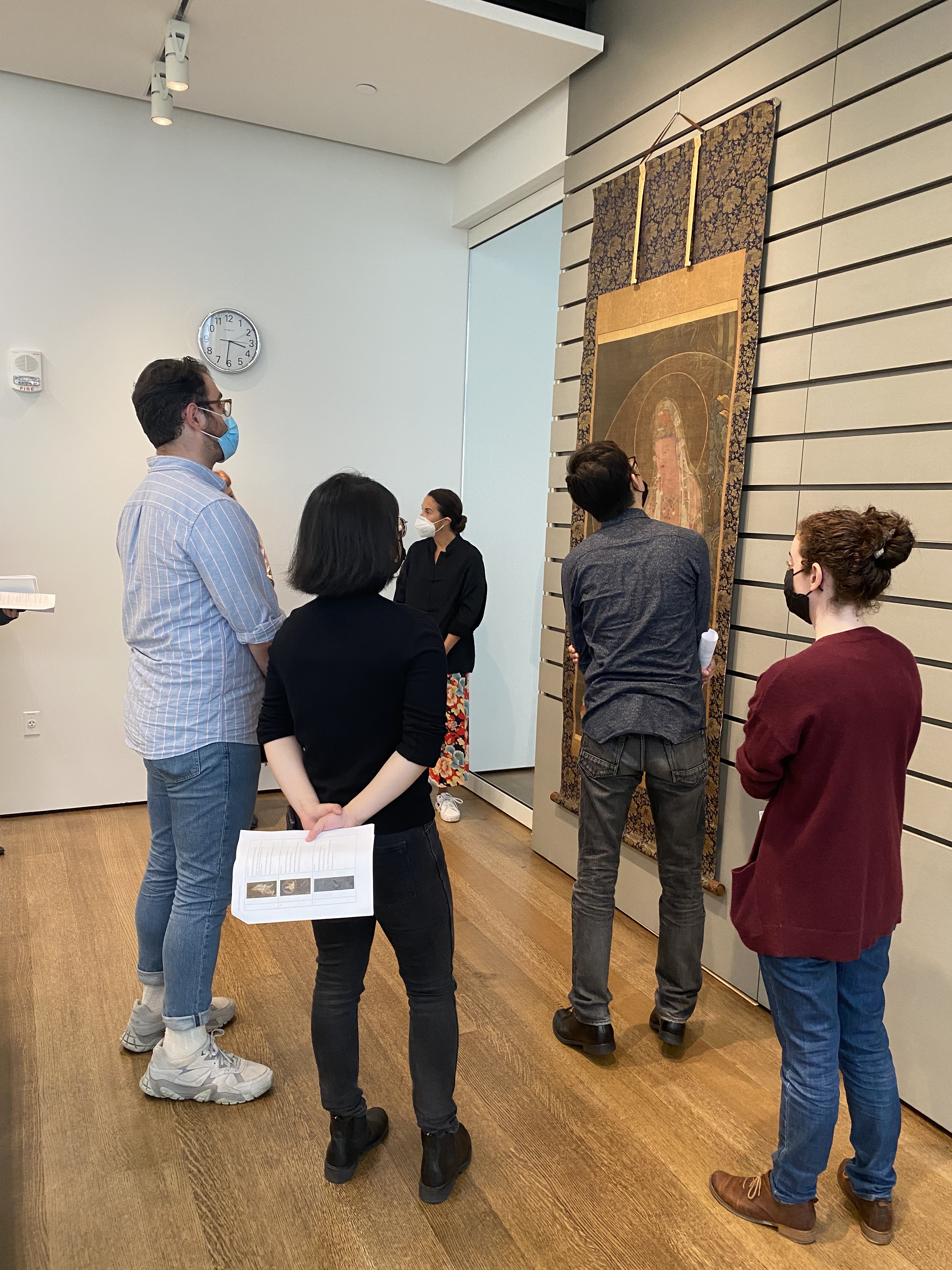 A group of students stand around a large scroll painting